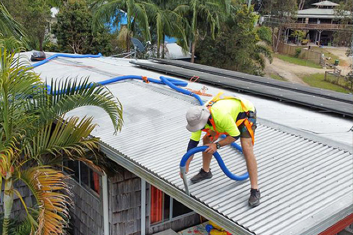 Man working on roof using an industrial vacuum cleaner, removing leaves and debris from gutter